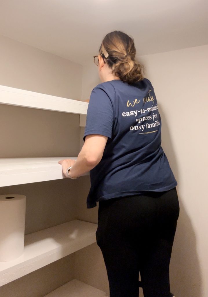 Andrea Brame in Nolensville Home Organizing shirt dusting off shelves in a walk-in pantry.